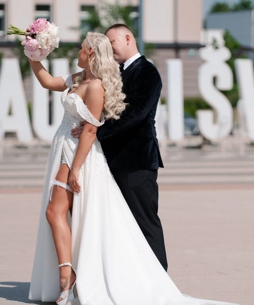 Nuotaka pakelia puokštę, jaunikis apkabina ją miesto aikštėje – vestuvių fotosesija Šiauliuose