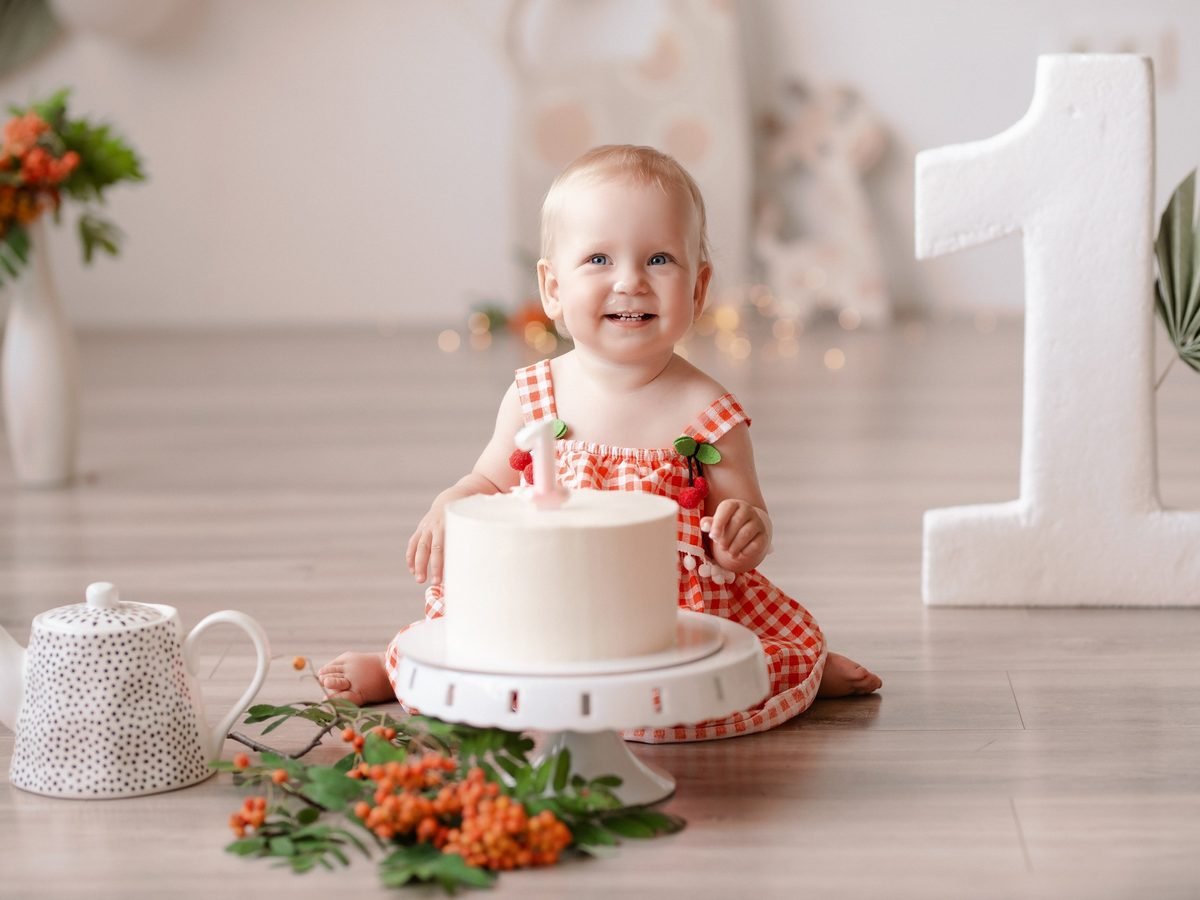 Kūdikė sėdi šalia balto torto su šermukšnio uogų šakelėmis – cake smash fotosesija Šiauliuose