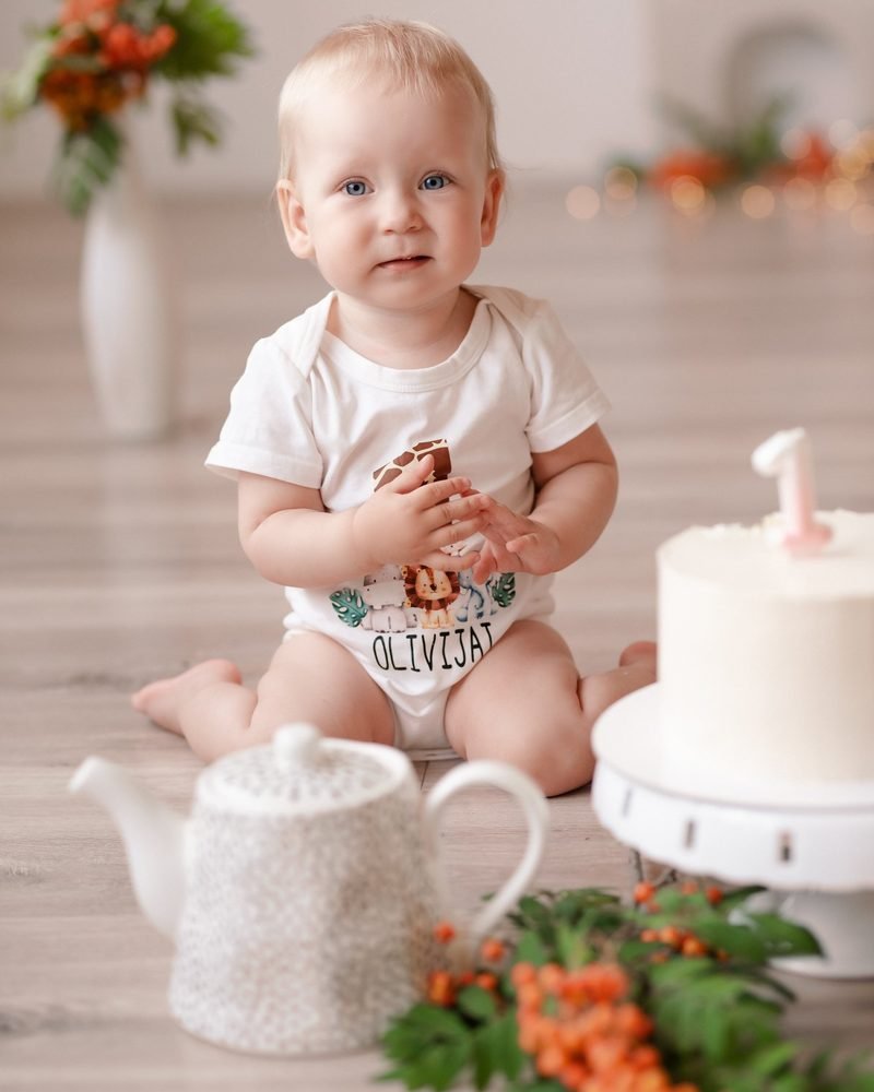 Kūdikis sėdi šalia torto su žvakute ir arbatinuko tarp uogų – cake smash fotosesija Šiauliuose