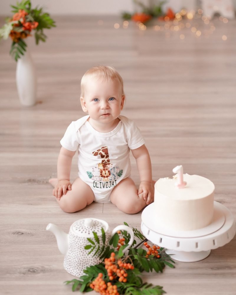 Kūdikis sėdi ant grindų šalia gimtadienio torto su žvake – cake smash fotosesija Šiauliuose