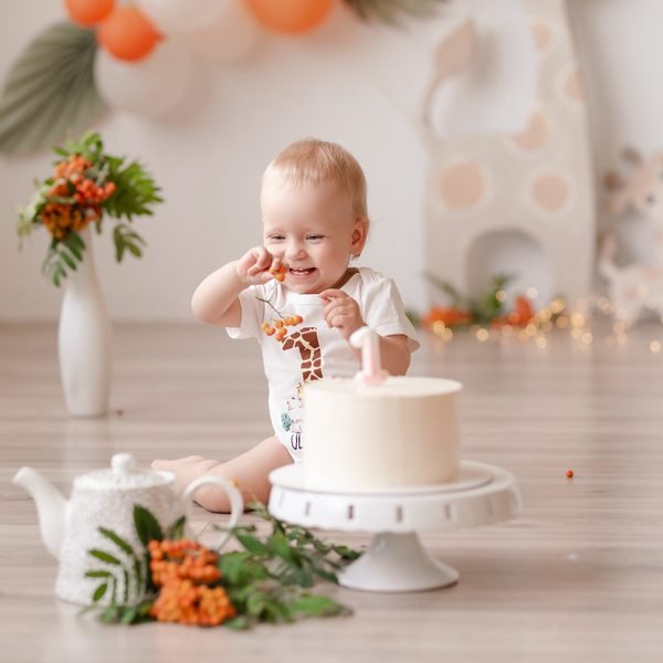 Kūdikis besijuokdamas valgo uogas šalia gimtadienio torto, fone balionai – Donatos Jankauskės fotografija, Šiauliai