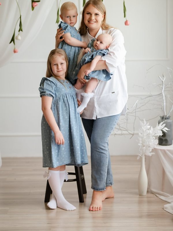 Mama laiko dvi mažas dukras ant rankų, šalia stovi vyresnioji dukra – šeimos fotosesija Šiauliuose