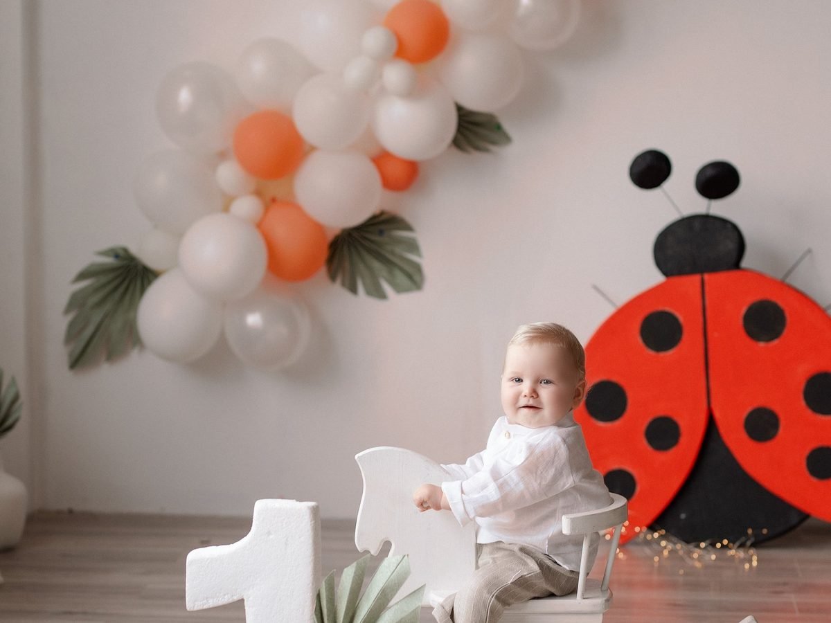 Berniukas sėdi ant žaislinio arkliuko prie balionų ir boružės dekoro – cake smash fotosesija Šiauliuose